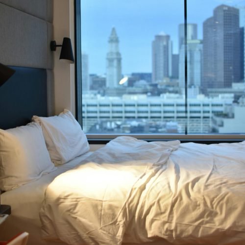 Modern hotel room overlooking Boston skyline, featuring luxury bedding.